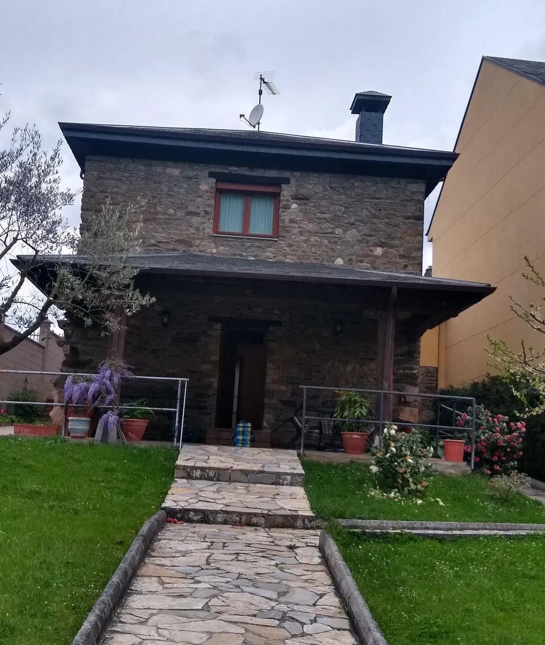Camino de losas hasta la entrada de la casa, con glicinia en flor