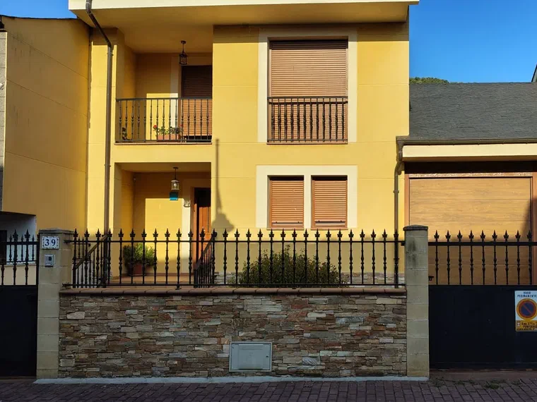 Fachada de la casa, de dos plantas, con verja de forja y muro de piedra